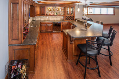 Example of a large classic l-shaped laminate floor and brown floor wet bar design in Other with an undermount sink, raised-panel cabinets, medium tone wood cabinets, laminate countertops, beige backsplash, terra-cotta backsplash and black countertops