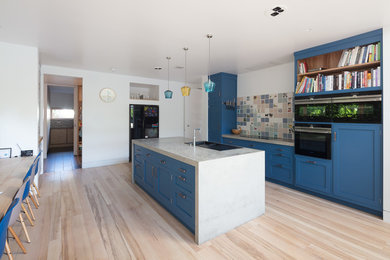 Inspiration for a large modern galley open plan kitchen in Hertfordshire with a drop-in sink, flat-panel cabinets, blue cabinets, solid surface benchtops, multi-coloured splashback, ceramic splashback, black appliances, light hardwood floors, with island and green benchtop.