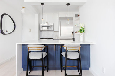 Modelo de cocinas en U contemporáneo con armarios estilo shaker, puertas de armario azules, una isla y encimeras blancas