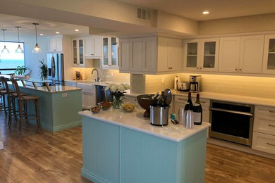Kitchen - coastal kitchen idea in Other with a farmhouse sink, recessed-panel cabinets, recycled glass countertops, glass tile backsplash, stainless steel appliances and two islands
