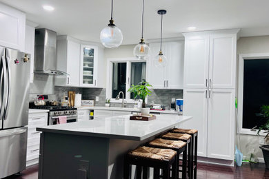ニューヨークにある高級な中くらいなモダンスタイルのおしゃれなキッチン (ドロップインシンク、フラットパネル扉のキャビネット、白いキャビネット、御影石カウンター、グレーのキッチンパネル、セラミックタイルのキッチンパネル、シルバーの調理設備、淡色無垢フローリング、茶色い床、白いキッチンカウンター) の写真