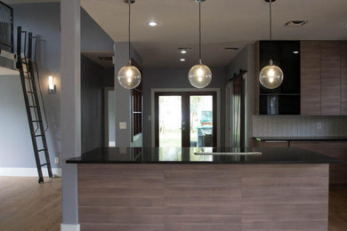 Inspiration for a large contemporary l-shaped medium tone wood floor and brown floor open concept kitchen remodel in Austin with an undermount sink, flat-panel cabinets, medium tone wood cabinets, granite countertops, gray backsplash, stainless steel appliances, an island and black countertops