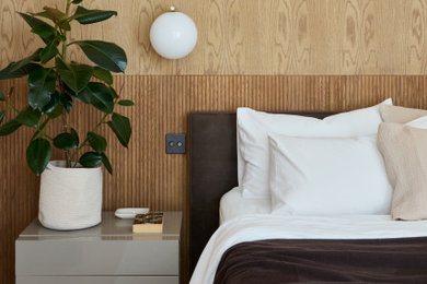 This is an example of a medium sized modern master and grey and pink bedroom in London with pink walls, light hardwood flooring, pink floors, wood walls and a feature wall.