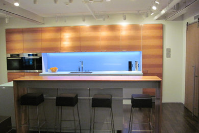 This is an example of a contemporary galley eat-in kitchen in Hawaii with an undermount sink, flat-panel cabinets, medium wood cabinets, solid surface benchtops, white splashback, glass sheet splashback and stainless steel appliances.