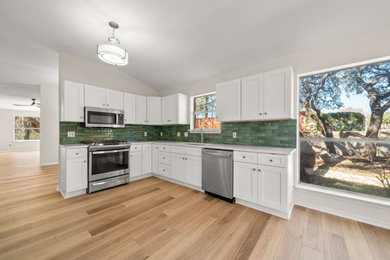Mid-sized transitional l-shaped vinyl floor and brown floor eat-in kitchen photo in Austin with an undermount sink, shaker cabinets, white cabinets, quartz countertops, green backsplash, porcelain backsplash, stainless steel appliances, no island and white countertops