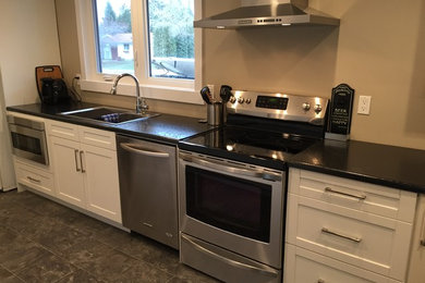 Mid-sized transitional single-wall eat-in kitchen in Calgary with a double-bowl sink, shaker cabinets, white cabinets, solid surface benchtops, white appliances, porcelain floors, no island and grey floor.