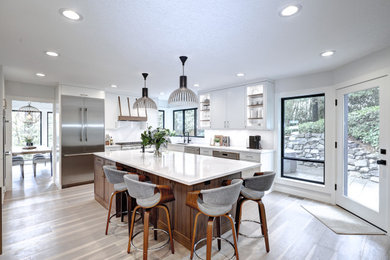 Large minimalist u-shaped medium tone wood floor and brown floor eat-in kitchen photo in Portland with an undermount sink, shaker cabinets, white cabinets, quartz countertops, white backsplash, quartz backsplash, stainless steel appliances, an island and white countertops