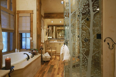 Inspiration for a large country master bathroom in Denver with an undermount sink, raised-panel cabinets, light wood cabinets, granite benchtops, an alcove tub, an alcove shower, a two-piece toilet, beige tile, stone tile, beige walls, light hardwood floors, brown floor and a hinged shower door.