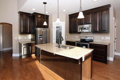 Open concept kitchen - traditional l-shaped medium tone wood floor open concept kitchen idea in Calgary with a double-bowl sink, raised-panel cabinets, dark wood cabinets, granite countertops, beige backsplash, porcelain backsplash, stainless steel appliances and an island