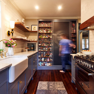 アトランタのトラディショナルスタイルのおしゃれなII型キッチン (エプロンフロントシンク、シェーカースタイル扉のキャビネット、青いキャビネット、白いキッチンパネル、サブウェイタイルのキッチンパネル、シルバーの調理設備、大理石カウンター、濃色無垢フローリング) の写真