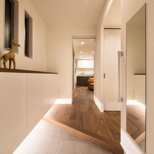 Immagine di un ingresso o corridoio design con pareti bianche, una porta grigia, pavimento marrone e pavimento in legno massello medio