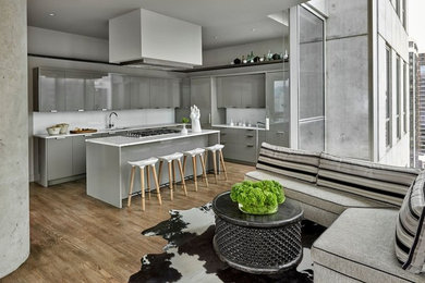 Design ideas for a large contemporary l-shaped open plan kitchen in Chicago with an undermount sink, flat-panel cabinets, grey cabinets, white splashback, light hardwood floors, with island and panelled appliances.