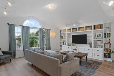 Mid-sized elegant enclosed laminate floor, brown floor and vaulted ceiling living room photo in Cincinnati with white walls and a media wall
