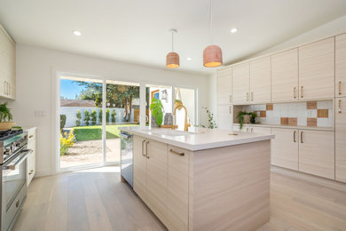 Mid-sized country galley eat-in kitchen in Los Angeles with an undermount sink, flat-panel cabinets, light wood cabinets, quartz benchtops, white splashback, ceramic splashback, stainless steel appliances, light hardwood floors, with island, grey floor and white benchtop.