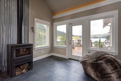 Photo of a beach style enclosed family room in Seattle with beige walls, slate floors, a wood stove, a metal fireplace surround and black floor.