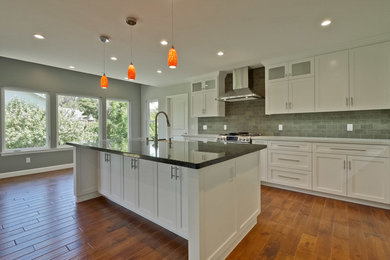 Eat-in kitchen - huge transitional l-shaped medium tone wood floor and brown floor eat-in kitchen idea in San Francisco with a farmhouse sink, shaker cabinets, white cabinets, granite countertops, green backsplash, stone tile backsplash, stainless steel appliances and an island