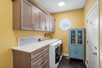 セントルイスにあるおしゃれなランドリールーム (黄色い壁、クッションフロア、左右配置の洗濯機・乾燥機、黒い床) の写真