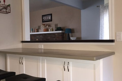 This is an example of a small contemporary l-shaped enclosed kitchen in Milwaukee with a double-bowl sink, shaker cabinets, white cabinets, composite countertops, black appliances, ceramic flooring and no island.