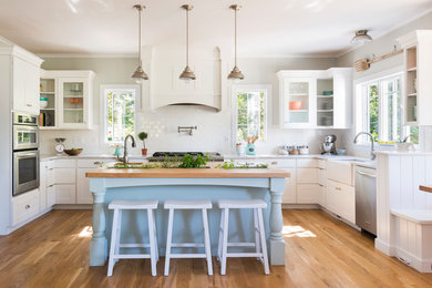 Inspiration for a farmhouse u-shaped medium tone wood floor kitchen remodel in Providence with a farmhouse sink, shaker cabinets, white cabinets, white backsplash, stainless steel appliances and an island