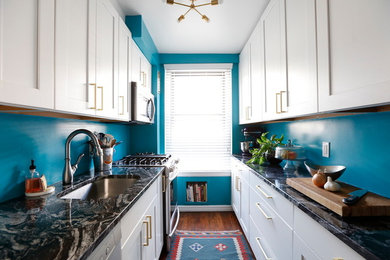 Example of a small transitional galley medium tone wood floor and brown floor enclosed kitchen design in New York with an undermount sink, shaker cabinets, white cabinets, quartzite countertops, stainless steel appliances, no island and black countertops