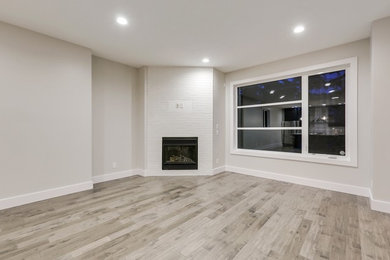 Example of a trendy open concept medium tone wood floor living room design in Calgary with white walls, a standard fireplace, a brick fireplace and a wall-mounted tv