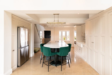 Inspiration for a large modern galley open plan kitchen in Hertfordshire with a belfast sink, shaker cabinets, green cabinets, engineered stone countertops, white splashback, engineered quartz splashback, black appliances, limestone flooring, an island, beige floors, white worktops, a coffered ceiling and a feature wall.