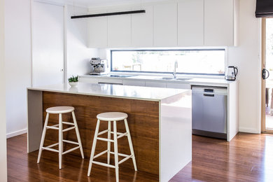 This is an example of a small modern galley open plan kitchen in Canberra - Queanbeyan with a double-bowl sink, flat-panel cabinets, white cabinets, quartz benchtops, window splashback, stainless steel appliances, bamboo floors, with island and brown floor.