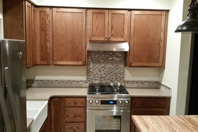 Eat-in kitchen - mid-sized traditional l-shaped ceramic tile eat-in kitchen idea in Denver with a farmhouse sink, shaker cabinets, medium tone wood cabinets, solid surface countertops, gray backsplash, matchstick tile backsplash, stainless steel appliances and an island