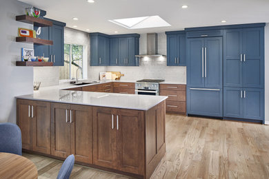 Example of a mid-sized trendy u-shaped light wood floor and brown floor eat-in kitchen design in Dallas with an undermount sink, recessed-panel cabinets, blue cabinets, marble countertops, white backsplash, ceramic backsplash, stainless steel appliances, a peninsula and white countertops