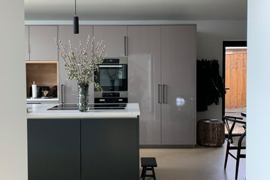 Inspiration for a large contemporary single-wall open plan kitchen in Buckinghamshire with a built-in sink, flat-panel cabinets, black cabinets, quartz worktops, concrete flooring, an island, brown floors, white worktops and a vaulted ceiling.