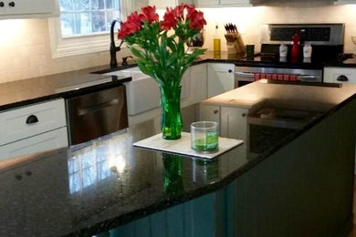 Example of a mid-sized cottage u-shaped light wood floor enclosed kitchen design in Other with a farmhouse sink, shaker cabinets, white cabinets, granite countertops, beige backsplash, stone tile backsplash, stainless steel appliances and an island