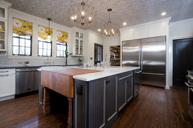 Photo of a transitional kitchen in Raleigh with a farmhouse sink, shaker cabinets, white cabinets, white splashback, stainless steel appliances, dark hardwood floors, with island, brown floor and white benchtop.