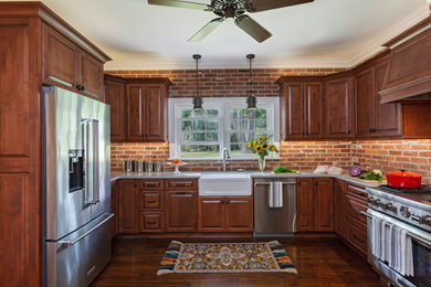 Example of a classic u-shaped dark wood floor enclosed kitchen design in Charleston with a farmhouse sink, raised-panel cabinets, dark wood cabinets, brick backsplash, stainless steel appliances and white countertops