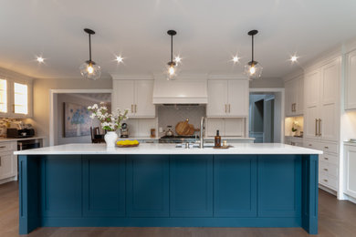 Example of a large transitional galley medium tone wood floor and brown floor eat-in kitchen design in Toronto with an undermount sink, recessed-panel cabinets, blue cabinets, quartz countertops, gray backsplash, porcelain backsplash, stainless steel appliances, an island and white countertops