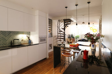 Exemple d'une grande cuisine ouverte parallèle industrielle avec un évier 1 bac, un placard à porte affleurante, des portes de placard blanches, une crédence verte, une crédence en céramique, un électroménager blanc, un sol en bois brun, un sol marron et plan de travail noir.