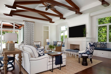 Photo of a large tropical open concept family room in Miami with white walls, a standard fireplace, a wall-mounted tv, brown floor and dark hardwood floors.