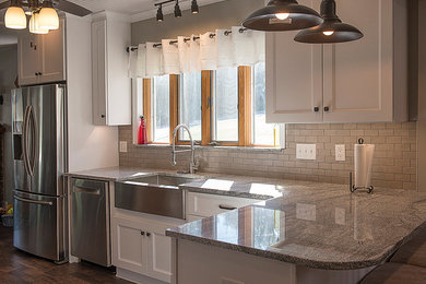 Example of a small mountain style l-shaped dark wood floor eat-in kitchen design in Other with a farmhouse sink, shaker cabinets, white cabinets, granite countertops, beige backsplash, ceramic backsplash, stainless steel appliances and a peninsula