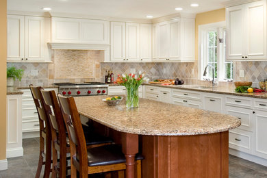 Inspiration for a large timeless l-shaped porcelain tile eat-in kitchen remodel in Boston with white cabinets, stainless steel appliances, an undermount sink, raised-panel cabinets, granite countertops, beige backsplash, stone tile backsplash and an island