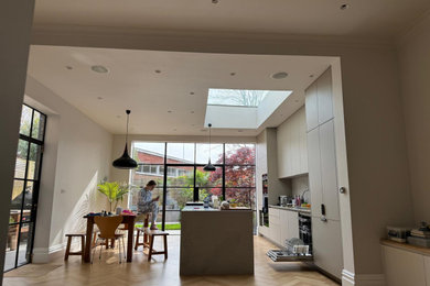 Photo of an expansive modern grey and white open plan kitchen in London with a submerged sink, beaded cabinets, grey cabinets, quartz worktops, white splashback, marble splashback, integrated appliances, an island, grey worktops, a drop ceiling and a feature wall.