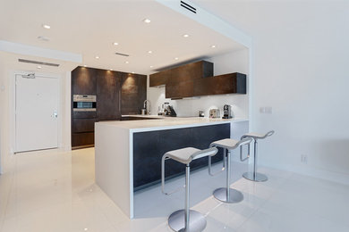 Example of a mid-sized minimalist l-shaped porcelain tile open concept kitchen design in Miami with an undermount sink, flat-panel cabinets, brown cabinets, white backsplash, stainless steel appliances, a peninsula and solid surface countertops