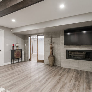 トロントの大きいトランジショナルスタイルのおしゃれな地下室 (半地下 (窓あり) 、グレーの壁、クッションフロア、吊り下げ式暖炉、コンクリートの暖炉まわり、茶色い床) の写真