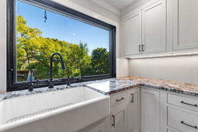 This is an example of a mid-sized modern l-shaped eat-in kitchen in Chicago with a farmhouse sink, shaker cabinets, white cabinets, quartzite benchtops, stainless steel appliances, light hardwood floors, with island, brown floor and white benchtop.