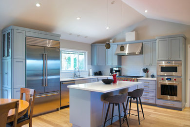 Photo of a large modern l-shaped open plan kitchen in San Francisco with an undermount sink, shaker cabinets, grey cabinets, quartz benchtops, white splashback, ceramic splashback, stainless steel appliances, light hardwood floors, with island, brown floor, white benchtop and vaulted.