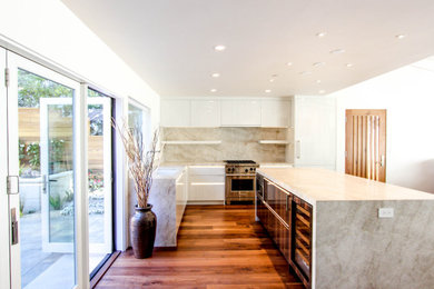 Offene, Große Moderne Küche in L-Form mit flächenbündigen Schrankfronten, braunem Holzboden, Kücheninsel und braunem Boden in Sonstige