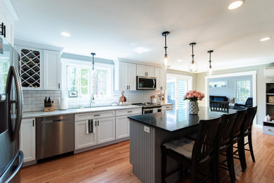 Eat-in kitchen - mid-sized traditional medium tone wood floor eat-in kitchen idea in Portland Maine with an undermount sink, recessed-panel cabinets, white cabinets, granite countertops, white backsplash, ceramic backsplash, stainless steel appliances, an island and gray countertops