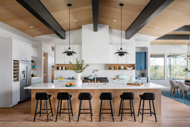 Huge mid-century modern medium tone wood floor, beige floor and wood ceiling eat-in kitchen photo in Austin with a drop-in sink, flat-panel cabinets, turquoise cabinets, quartz countertops, white backsplash, porcelain backsplash, stainless steel appliances, an island and white countertops