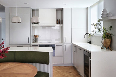 Small scandinavian l-shaped kitchen in Brisbane with an undermount sink, beaded inset cabinets, grey cabinets, quartz benchtops, white splashback, engineered quartz splashback, black appliances, light hardwood floors, with island, brown floor and white benchtop.