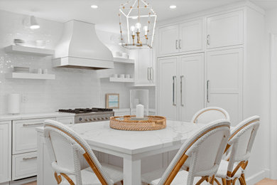 Example of a beach style l-shaped light wood floor and beige floor kitchen design in Miami with shaker cabinets, white cabinets, white backsplash, subway tile backsplash, paneled appliances, an island and white countertops