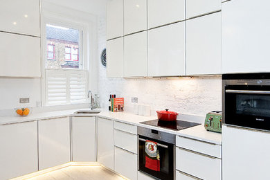This is an example of a contemporary l-shaped kitchen in London with flat-panel cabinets, white cabinets, white splashback, light hardwood floors, no island and white benchtop.