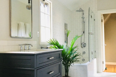 Mid-sized transitional white tile and porcelain tile mosaic tile floor, white floor and single-sink tub/shower combo photo in San Francisco with shaker cabinets, gray cabinets, a one-piece toilet, gray walls, an integrated sink, solid surface countertops, a hinged shower door, white countertops, a niche and a freestanding vanity